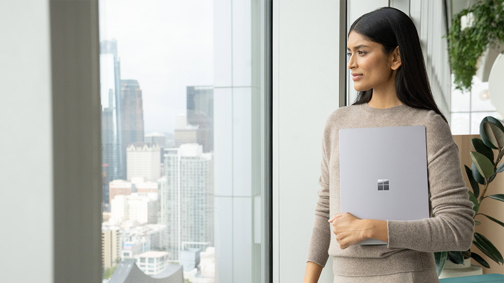 一个人单手拿着 Surface Laptop 5 商用版同时望向窗外。